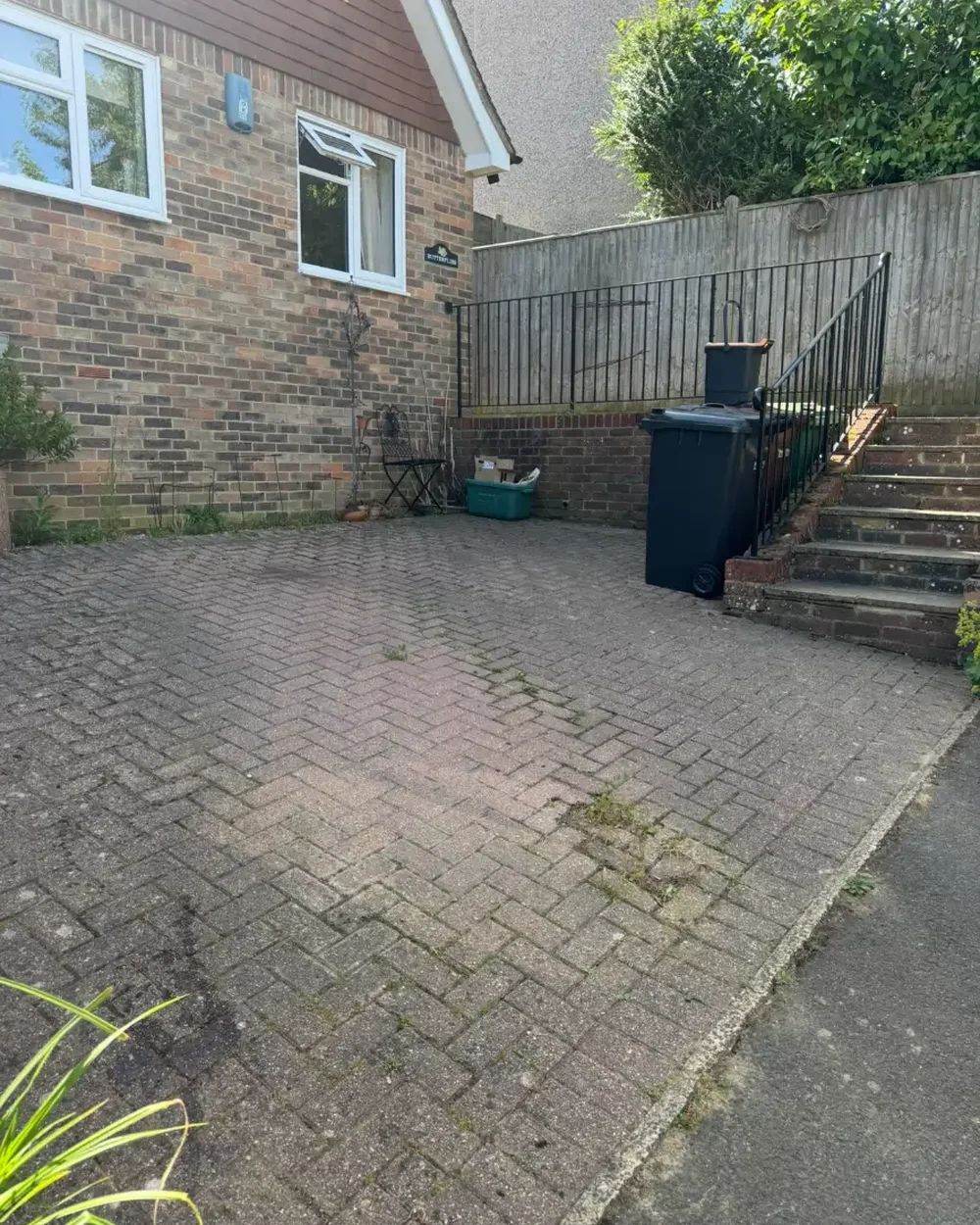 Block paved parking area behind a house with moss and weed growth before cleaning