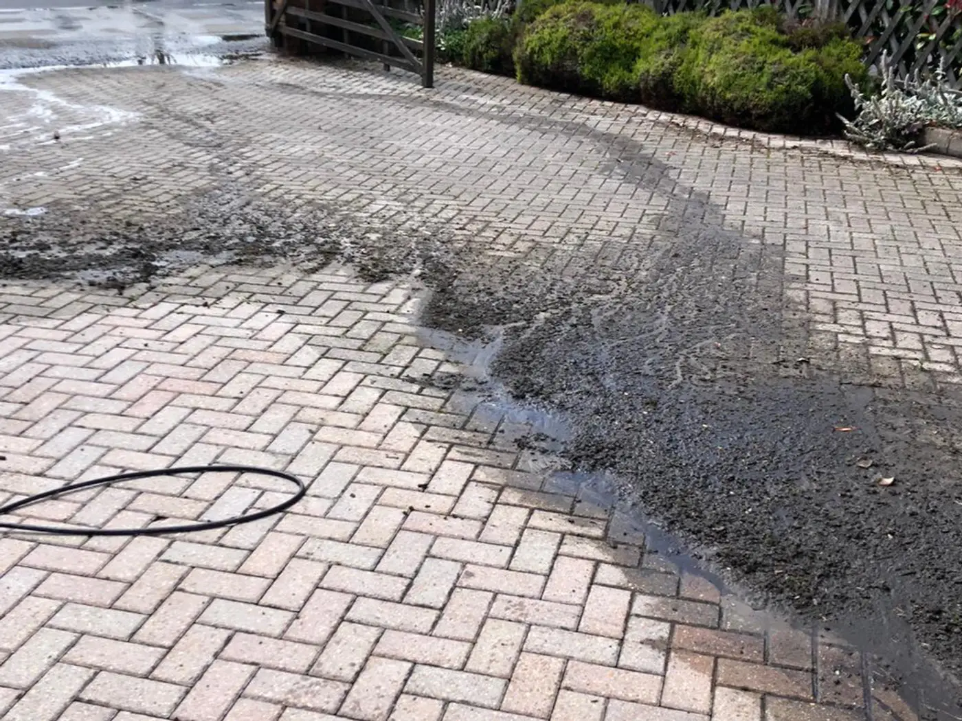 Block paving driveway being pressure washed, dirty water running off the cleaned section