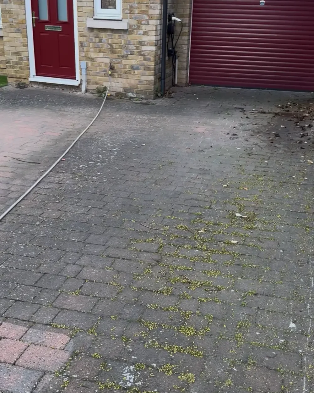 Red block paved driveway in front of a double garage, dulled by moss before cleaning